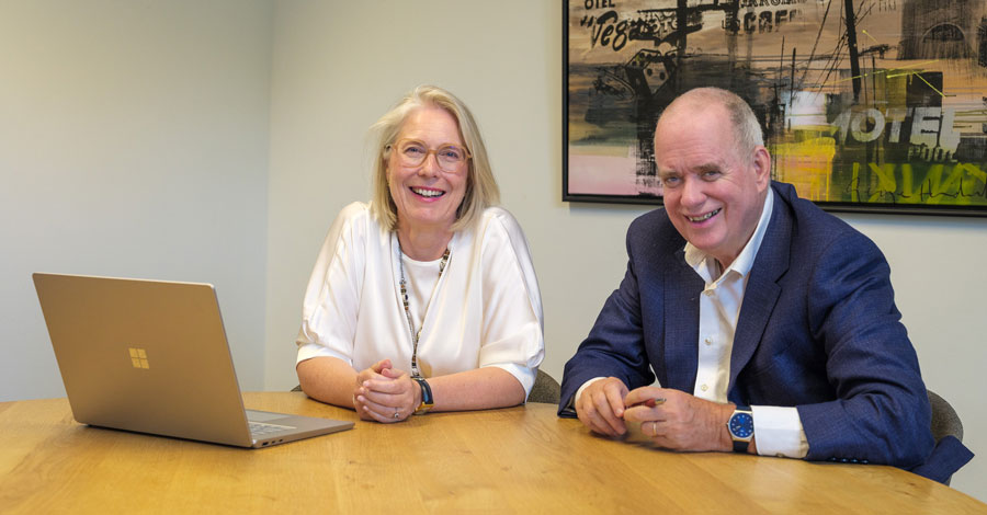 Een man en vrouw zitten aan een tafel met een laptop; zij zijn de eigenaren van het bedrijf.