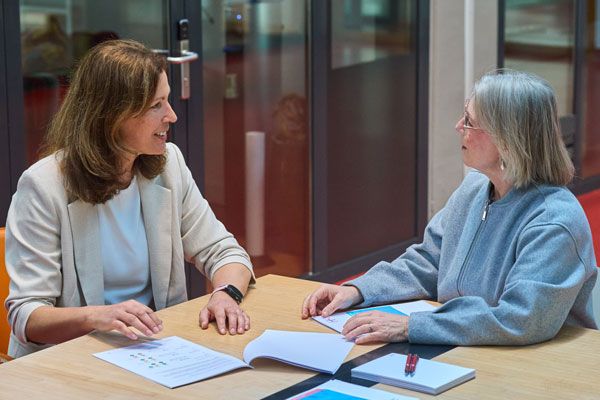 Twee vrouwen zitten aan een tafel en voeren een gesprek met elkaar.