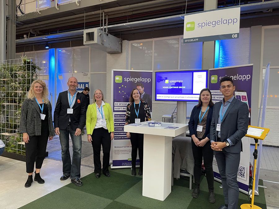 Een groep mensen staat voor een tafel, met verschillende voorwerpen op de tafel en een informele sfeer.