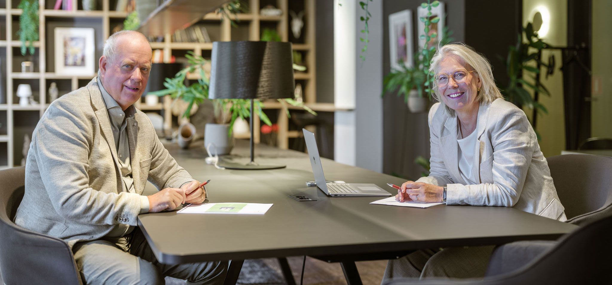 Een man en vrouw zitten aan een tafel met een laptop; zij zijn de eigenaren van het bedrijf.